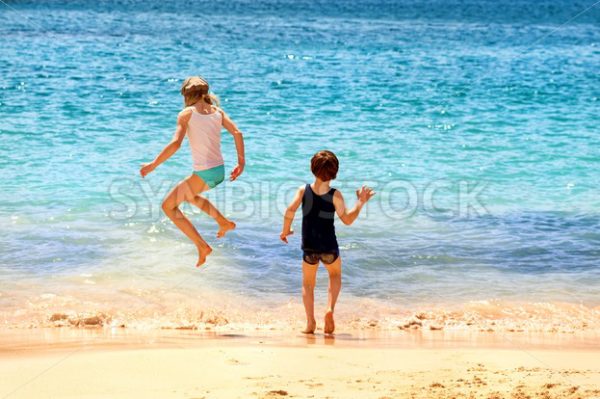 Two kids jumping in the sea waves on a sand beach - GlobePhotos - royalty free stock images